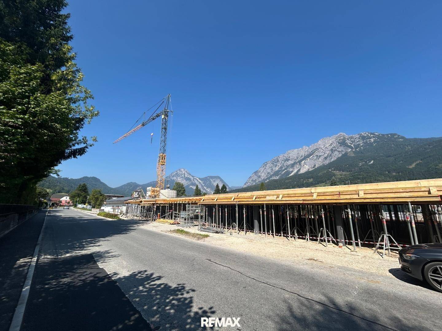 Baustelle mit Schalung und Kran vor einer beeindruckenden Bergkulisse an einem sonnigen Tag.