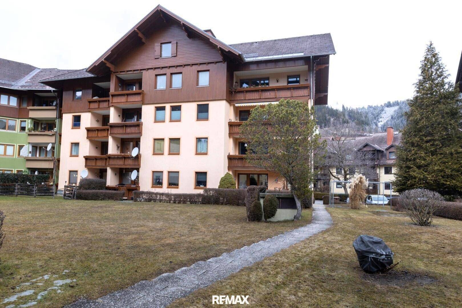 Mehrfamilienhaus mit gepflegter Rasenfläche und Bergkulisse im Hintergrund.