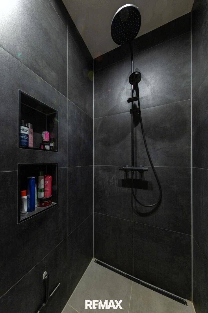 Moderne Dusche mit dunklen Fliesen, Regenduschkopf und integrierten Nischen.