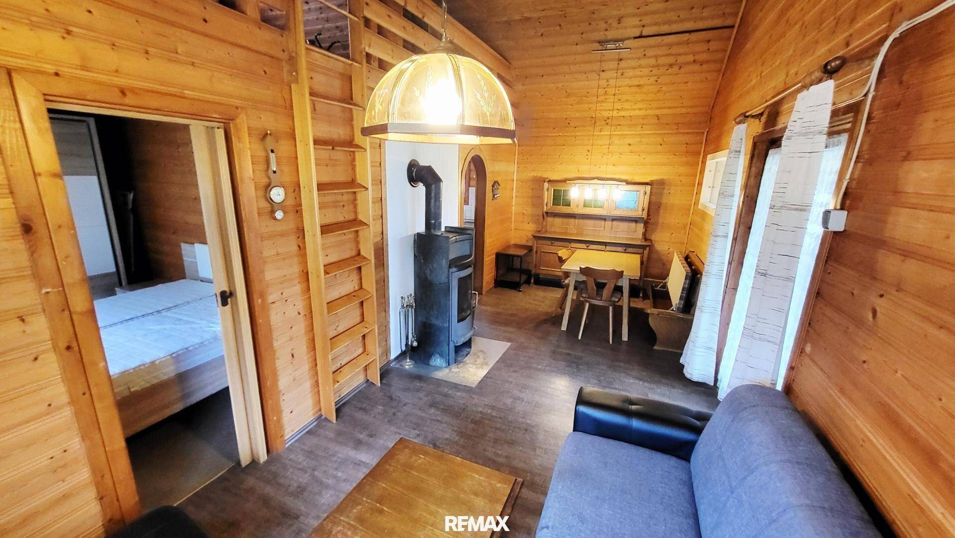 Wohnzimmer mit Holzofen, Sofa und Zugang zu einem weiteren Schlafzimmer.