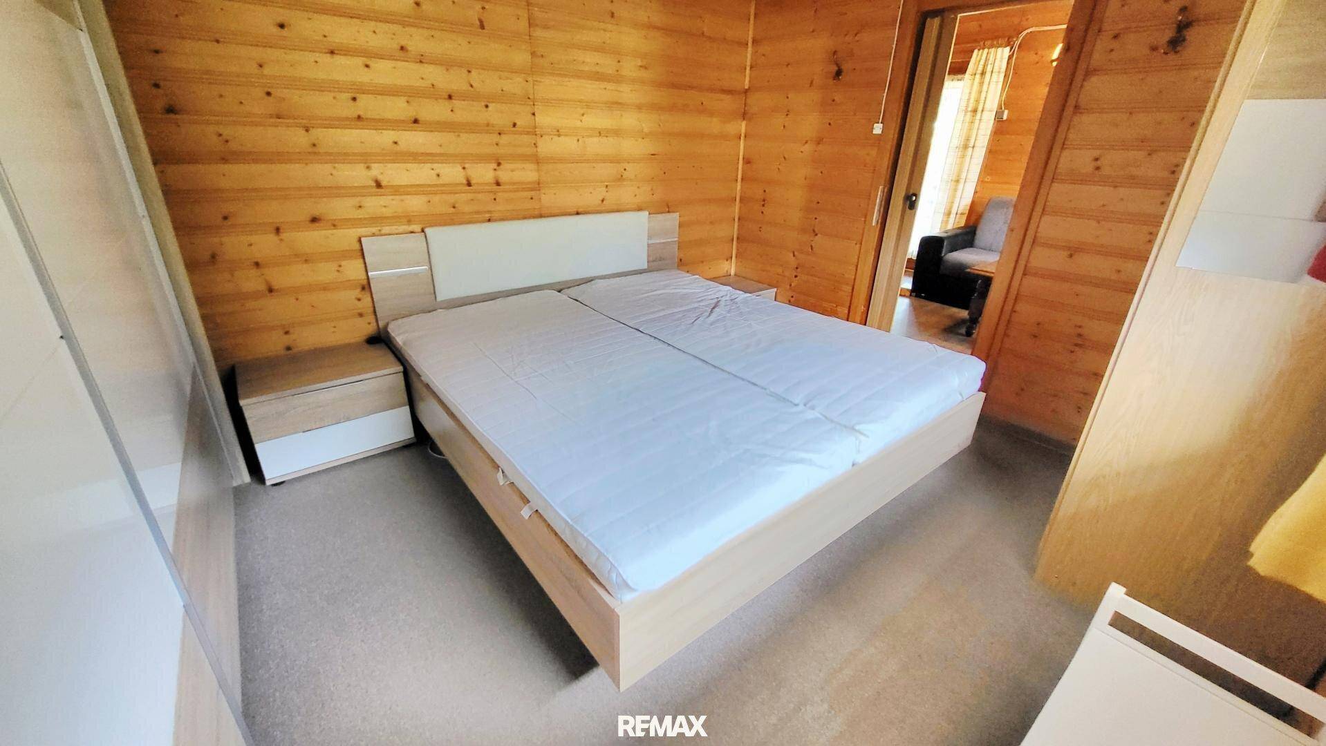 Helles Schlafzimmer mit Holzwänden, Doppelbett und Nachttischen.