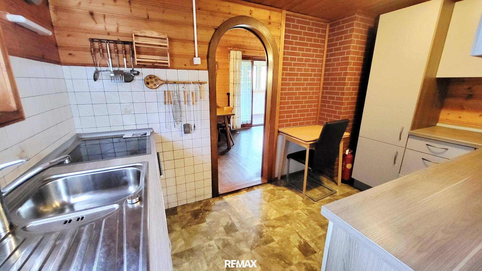Rustikale Küche mit Holzvertäfelung, einfacher Ausstattung und Durchgang zum Essbereich.