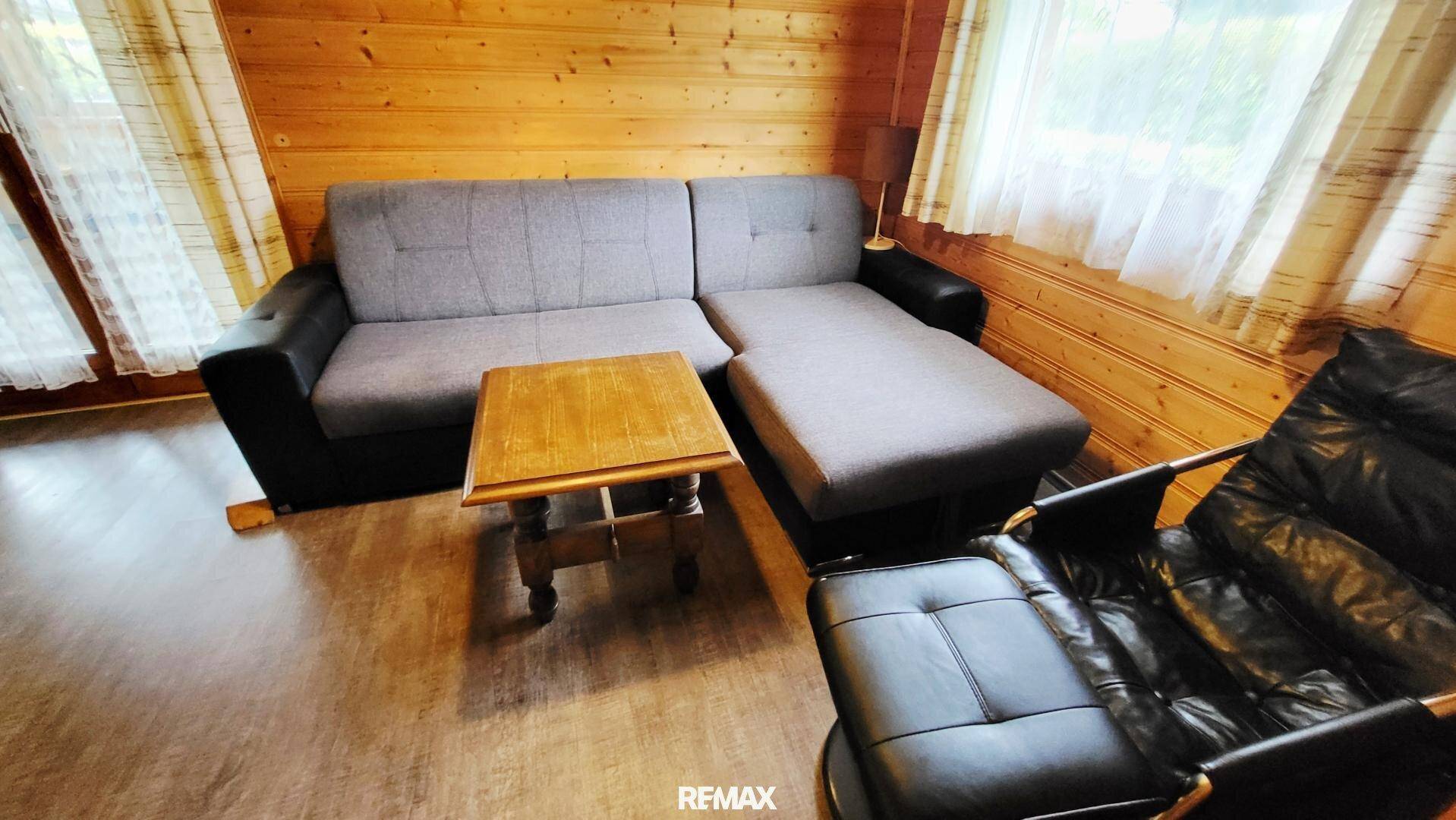 Gemütliches Wohnzimmer mit Sofa, Sessel und Holztisch in rustikalem Ambiente.