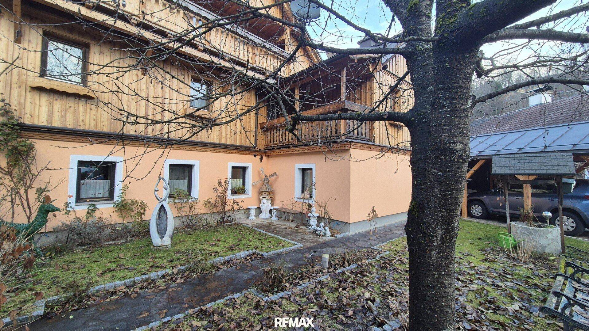 Traditionelles Holzhaus mit verputzter Fassade, kleinem Vorgarten und Holzbalkon.