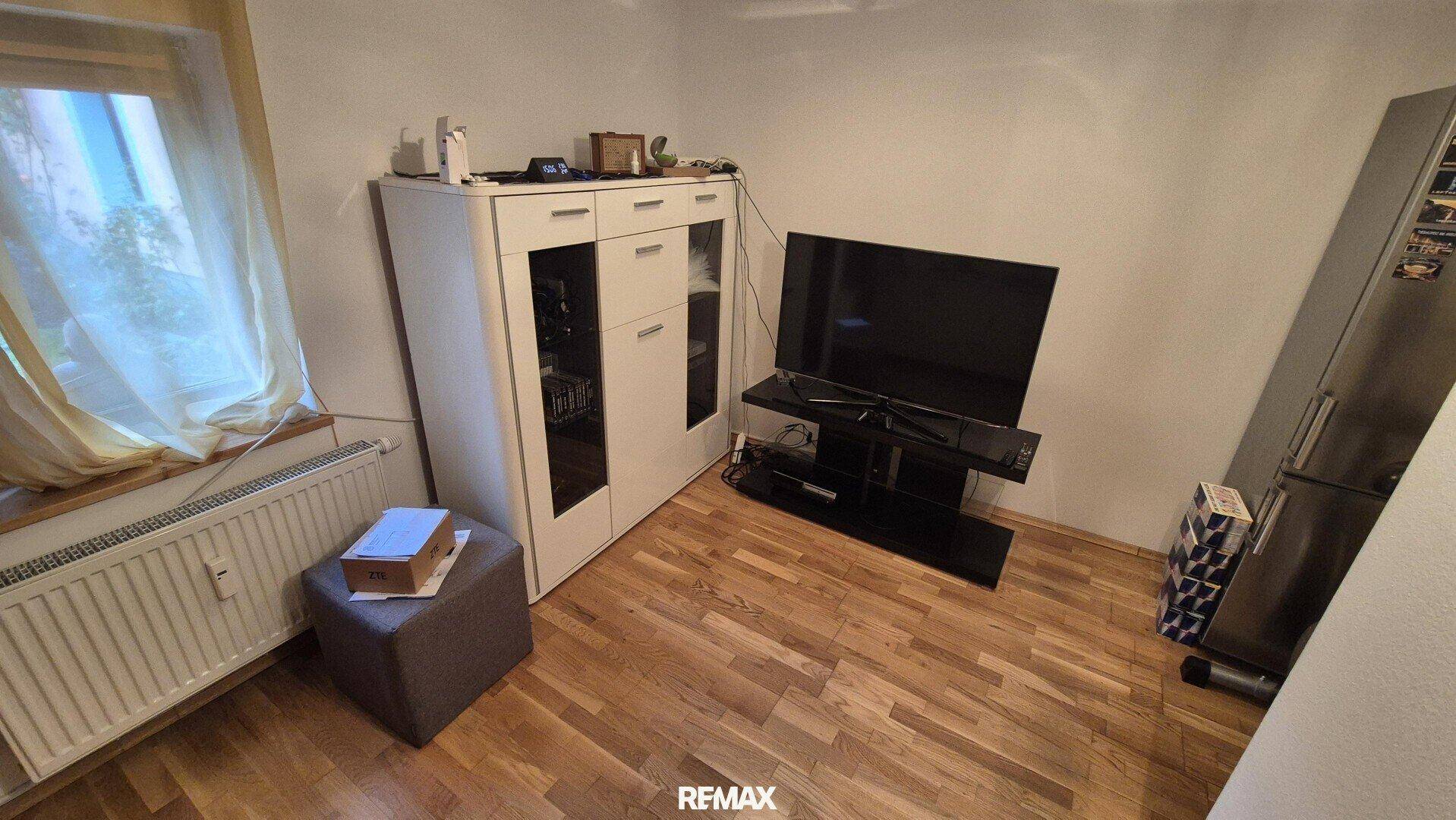 Wohnbereich mit Fernseher, Schrank und Fenster, ausgestattet mit Laminatboden.