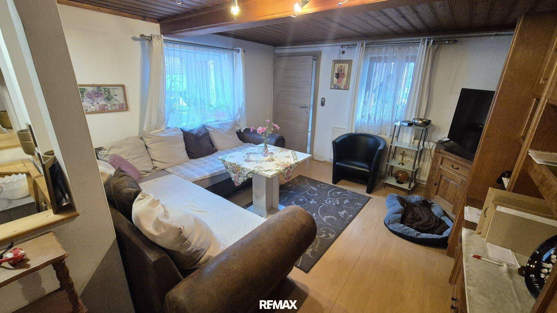 Gemütliches Wohnzimmer mit Holzbalkendecke, bequemer Eckcouch und Holzofen.