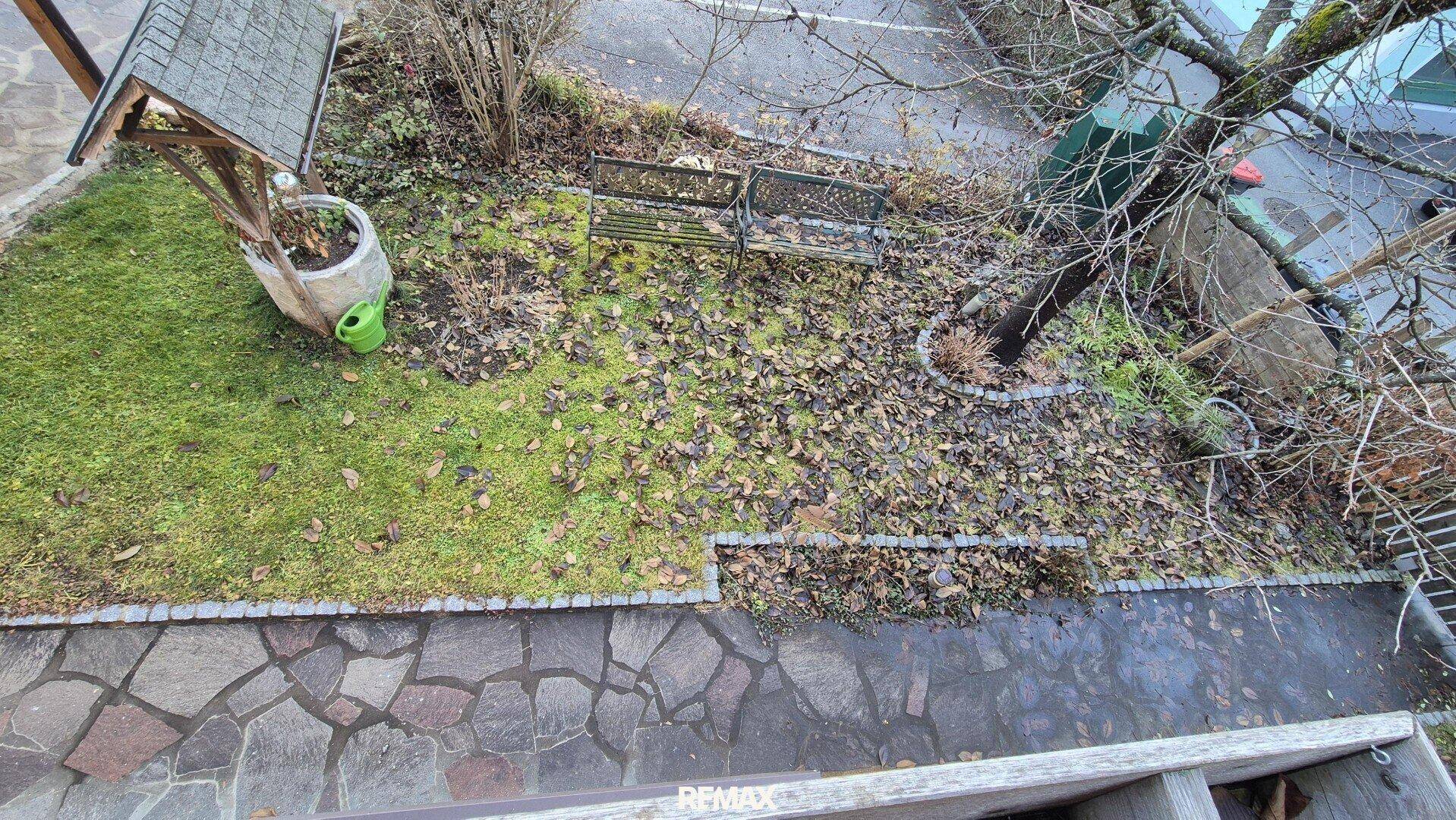 Gartenbereich mit Rasenfläche, Bäumen und einem gepflasterten Weg von oben betrachtet.