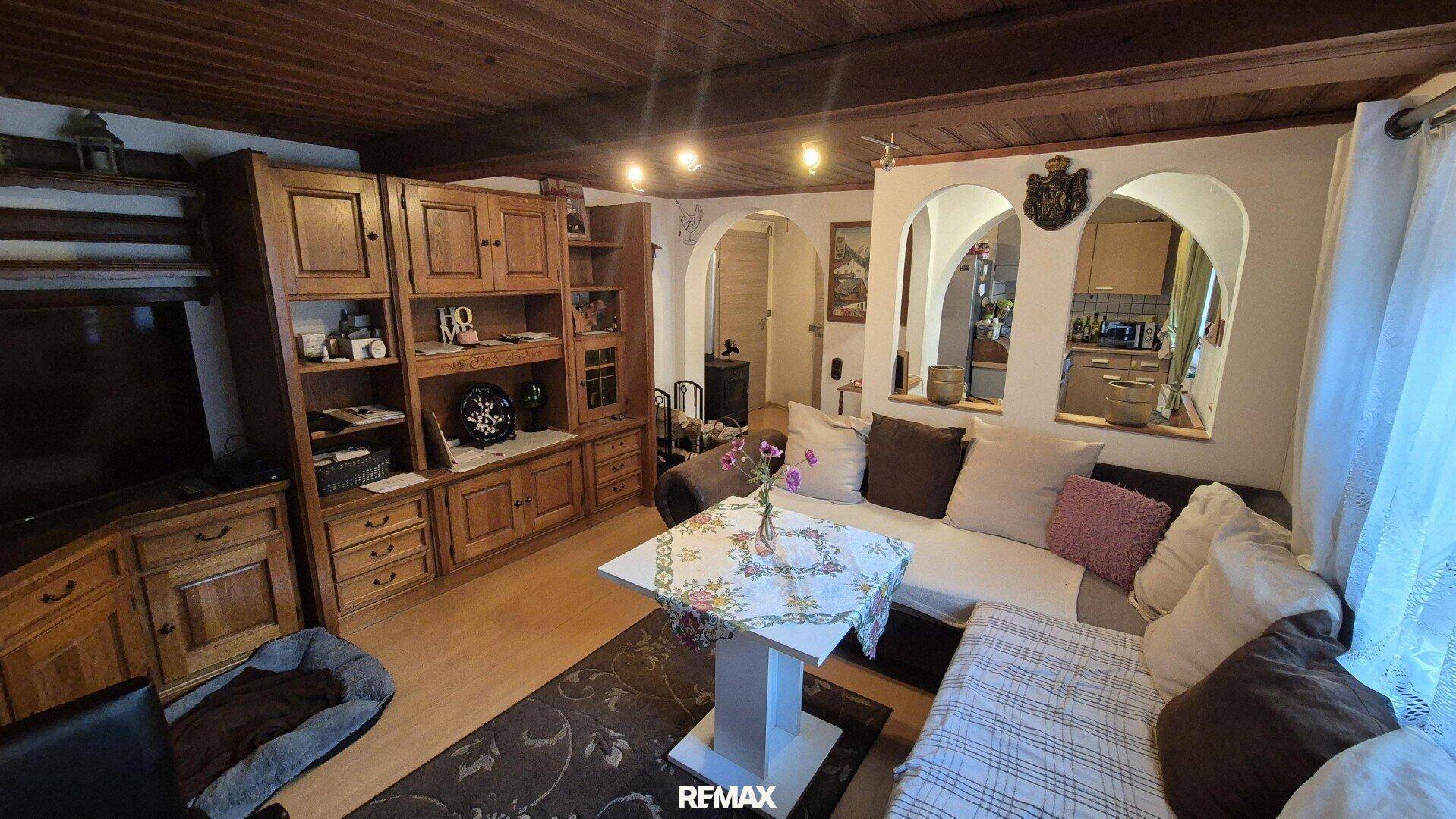 Traditionelles Wohnzimmer mit Holzbalkendecke, großem Holzschrank und Durchgang zur Küche.