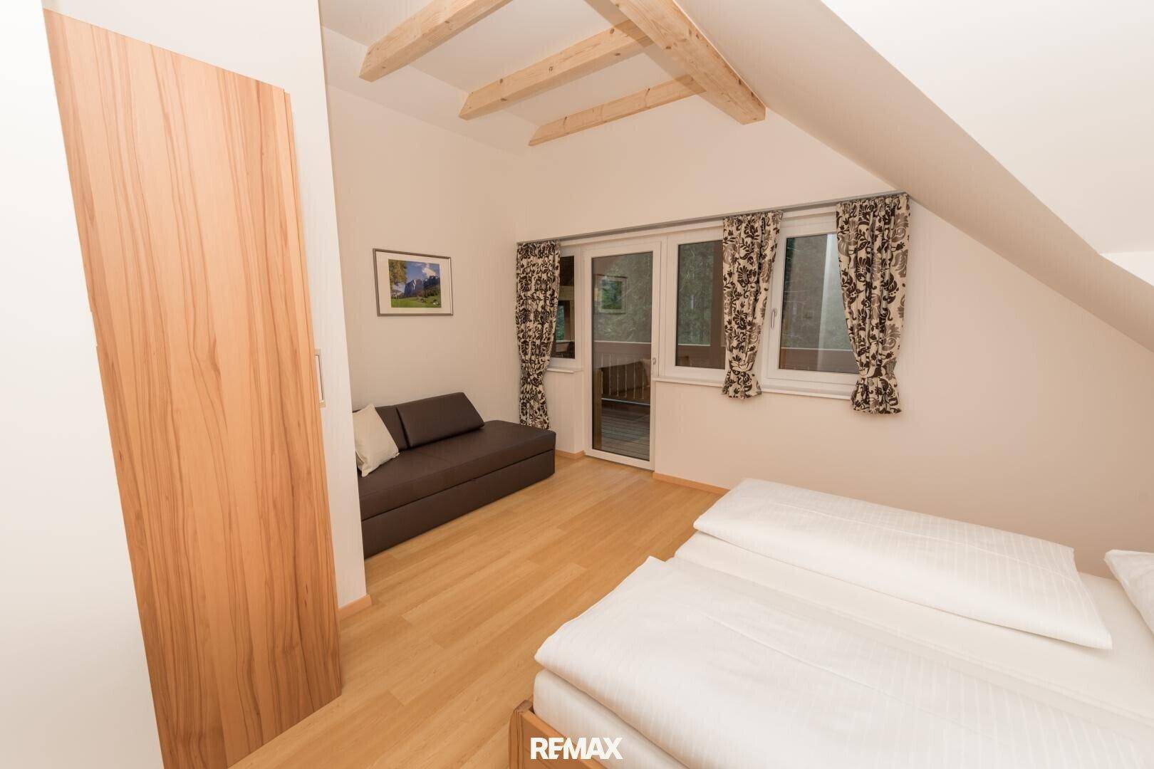 Gemütliches Schlafzimmer mit Doppelbett, Schlafsofa und Zugang zu einem kleinen Balkon.