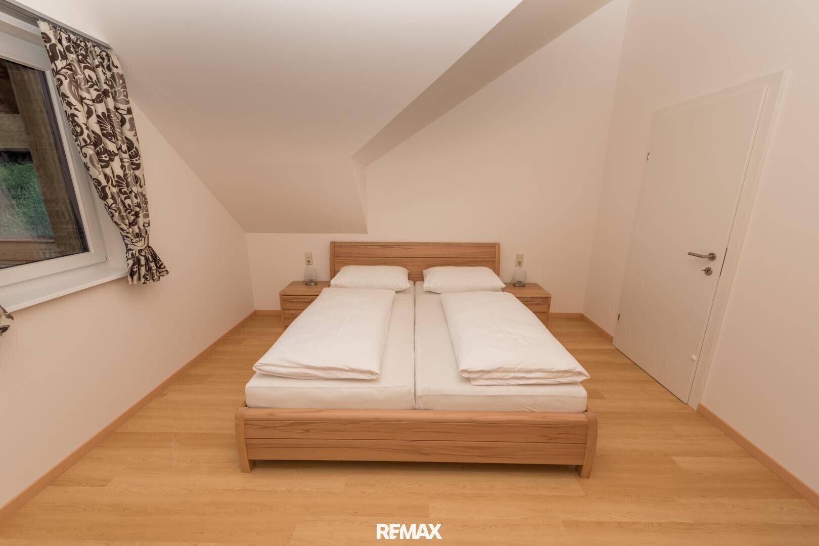 Gemütliches Schlafzimmer mit Doppelbett aus Holz, Nachttischen und schrägen Decken.