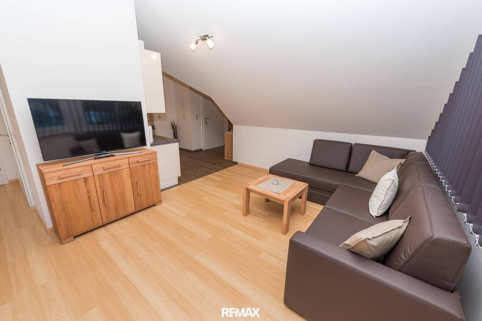 Geräumiger Wohnbereich mit bequemer Eckcouch, Fernseher und hellem Laminatboden.