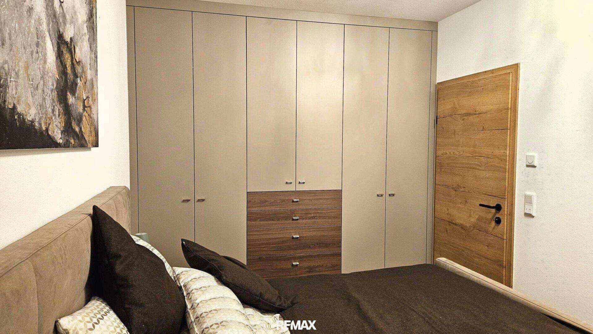 Schlafzimmer mit integrierten Kleiderschränken und Holztür, bietet viel Stauraum und modernes Design.