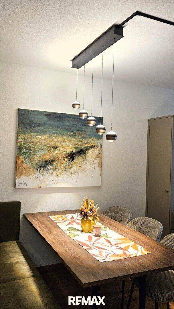 Moderner Essbereich mit stilvoller Pendelleuchte über dem Holztisch und Kunstwerk, elegant und einladend.