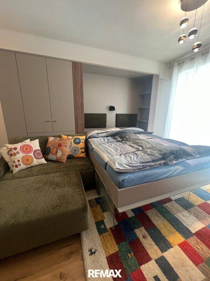 Flexibler Wohnbereich mit Schlafsofa und farbenfrohem Teppich, ideal für Gäste und gemütliche Abende.