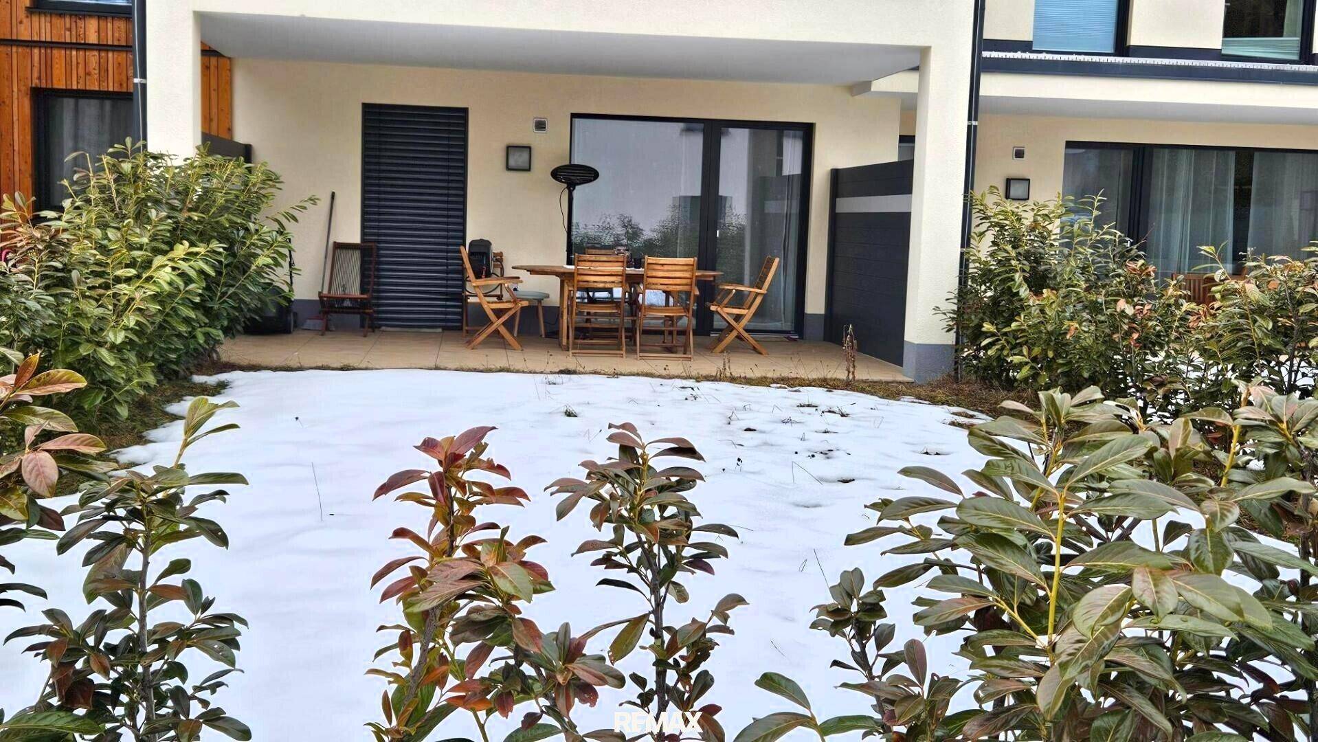 Geräumige Terrasse mit Holztisch und Stühlen, umgeben von Schnee und Sträuchern, ideal für Outdoor-Momente.