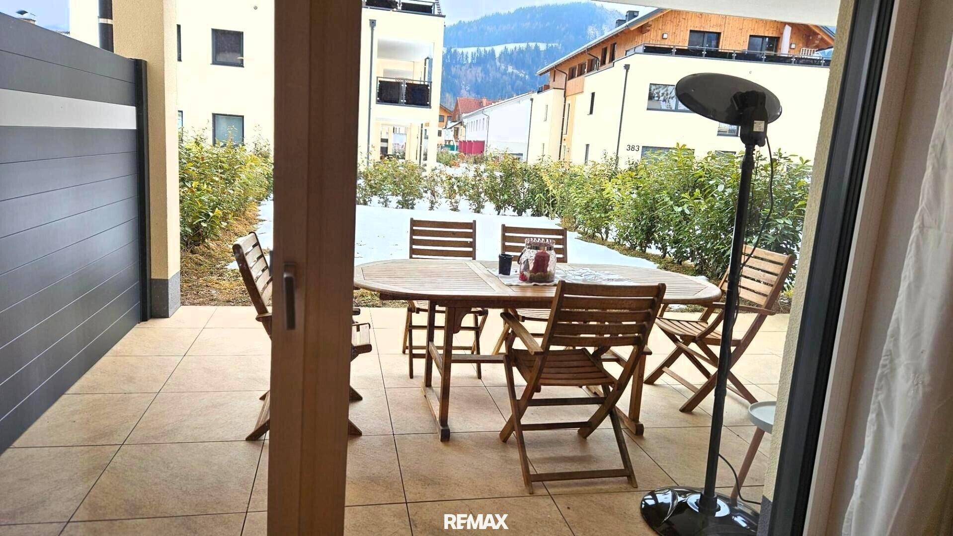 Blick von innen auf die möblierte Terrasse mit Heizstrahler und verschneitem Garten, einladend und gemütlich.