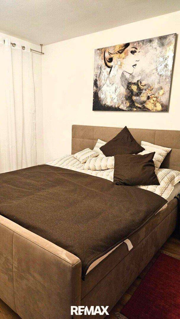 Gemütliches Schlafzimmer mit großem Bett, dunkler Bettwäsche und Kunstwerk an der Wand, ruhig und einladend.