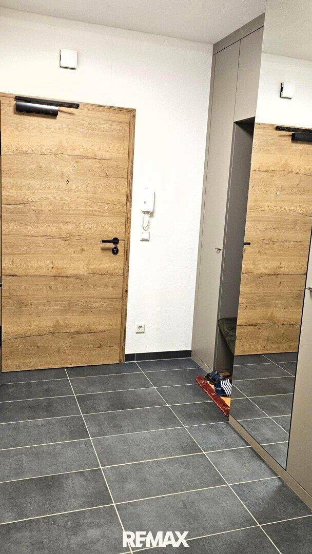 Moderner Eingangsbereich mit Holztür, grauen Fliesenboden und einem großen Spiegelschrank.
