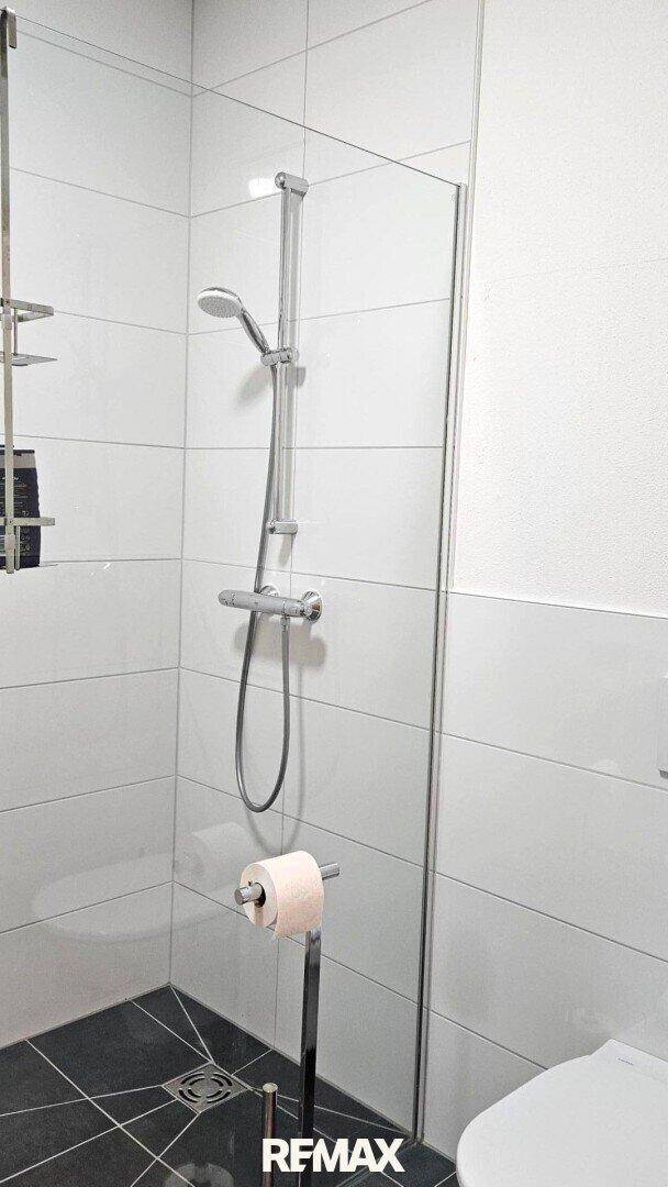 Helle Duschkabine mit Glasabtrennung und modernem WC in weiß gefliestem Bad, funktional und sauber.