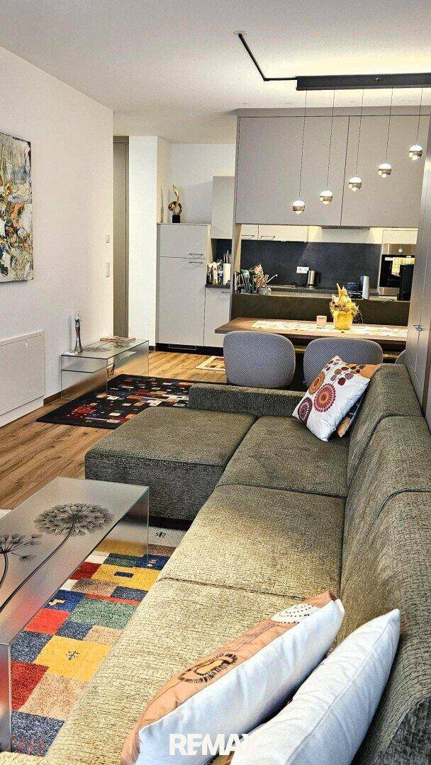 Komfortabler Wohnbereich mit Ecksofa und farbenfrohem Teppich, offen zum Essbereich und Küche.