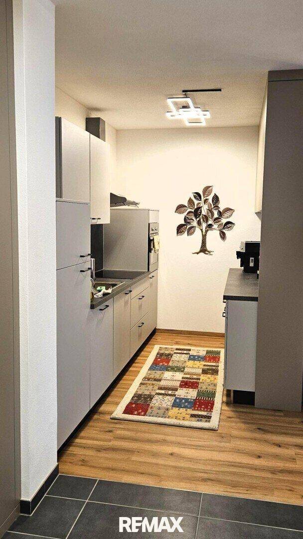 Funktionale Küche mit hellen Schränken, Holzboden und farbenfrohem Teppich, gut ausgestattet.