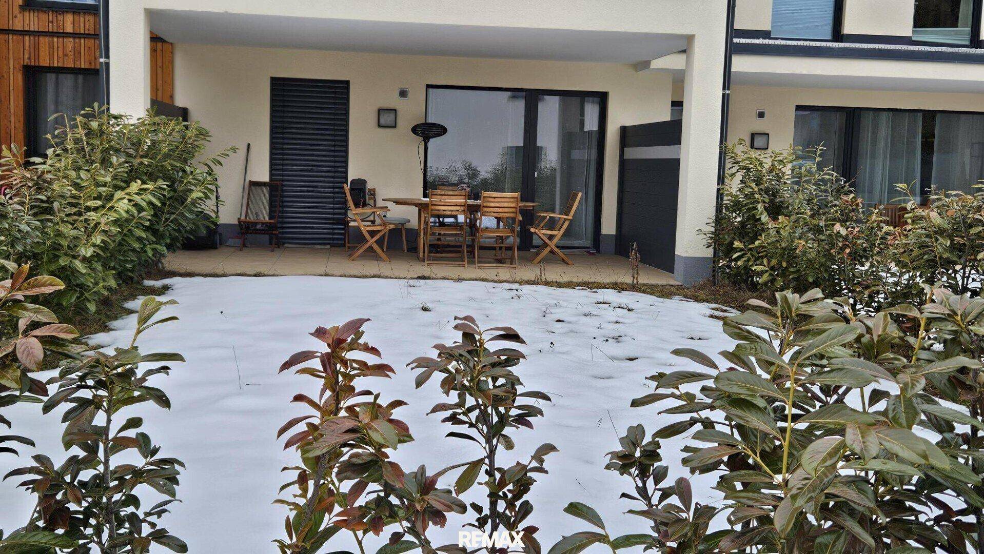 Geräumige Terrasse mit Holztisch und Stühlen, umgeben von Schnee und Sträuchern, ideal für Outdoor-Momente.