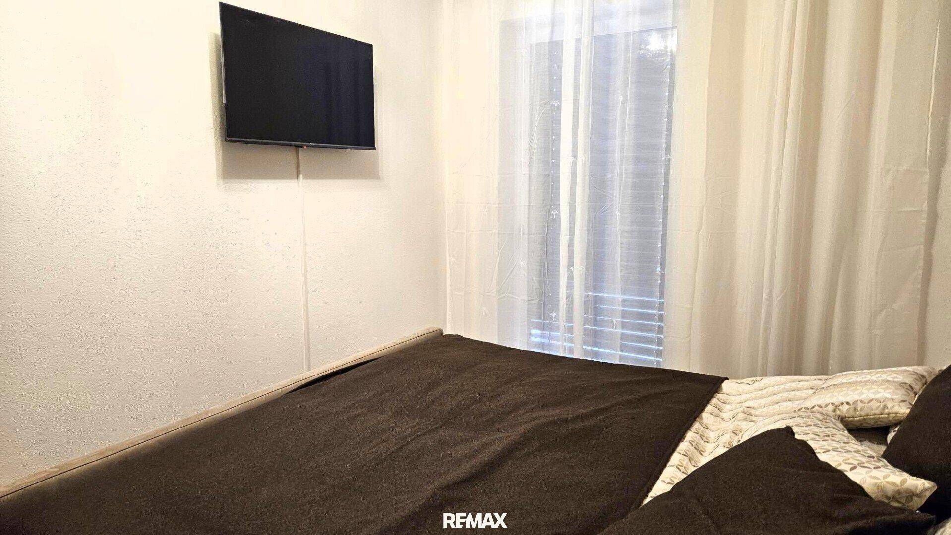 Schlafzimmer mit Wandfernseher und Fenster mit Vorhängen, bietet Komfort und Privatsphäre.