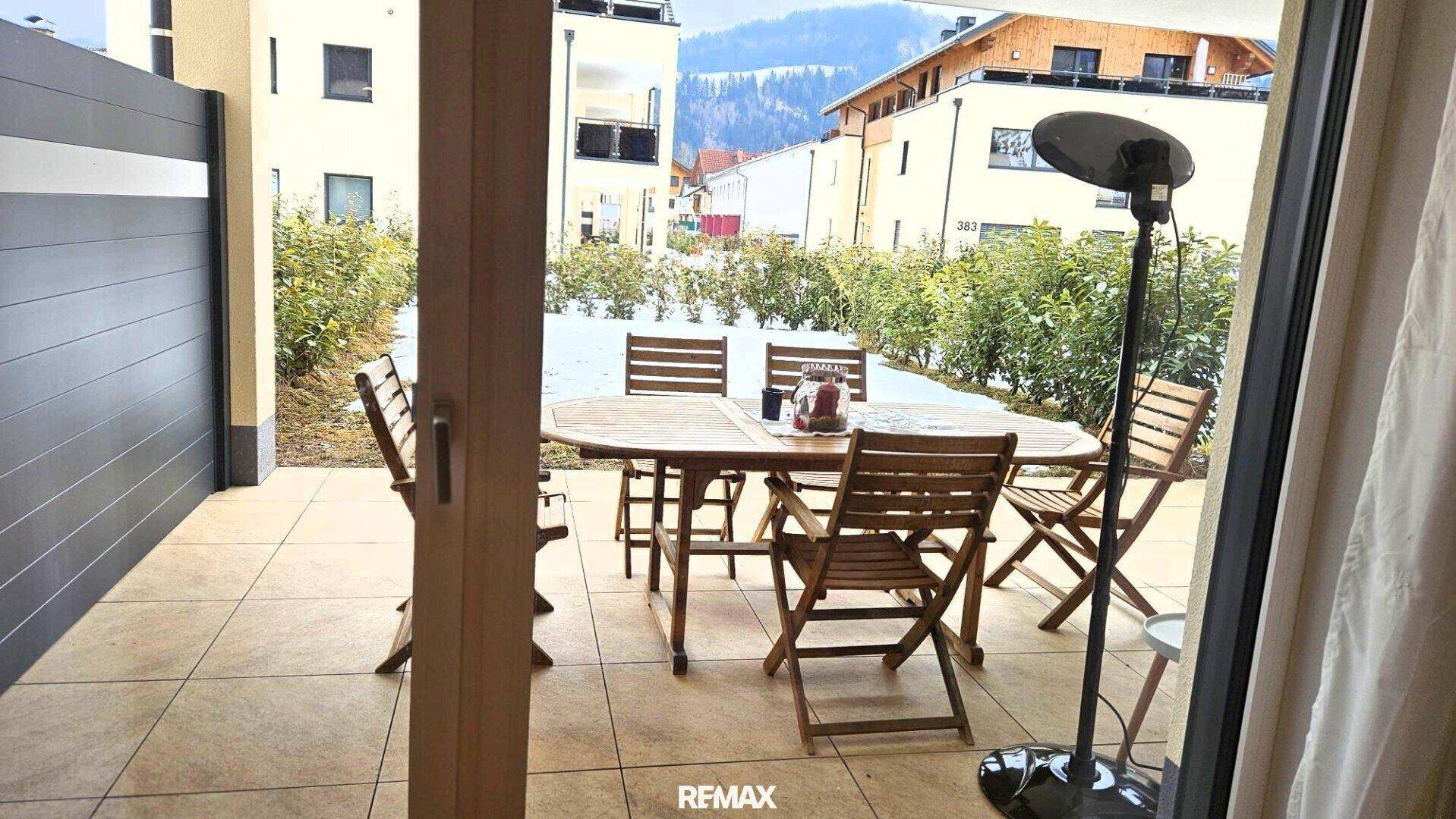 Blick von innen auf die möblierte Terrasse mit Heizstrahler und verschneitem Garten, einladend und gemütlich.