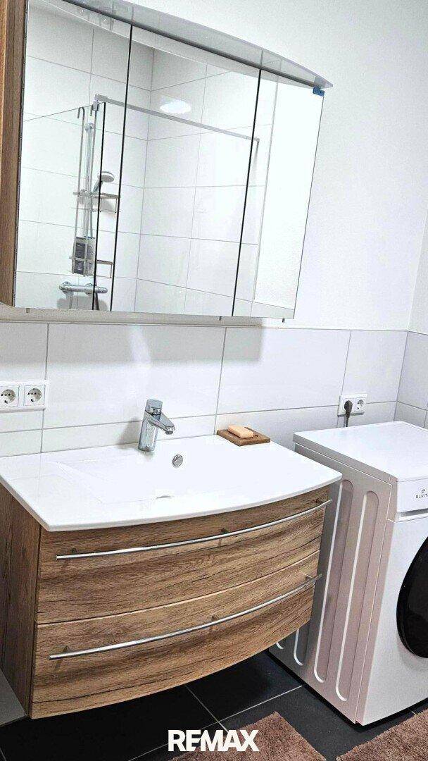 Modernes Badezimmer mit Holzwaschtisch, Spiegelschrank und integrierter Waschmaschine, praktisch und hell.