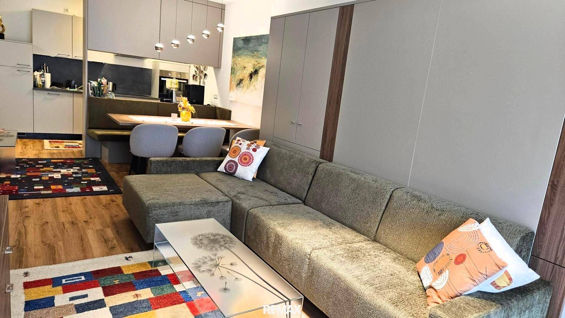Gemütlicher Wohn-Essbereich mit Sofa, Esstisch und offener Küche im Hintergrund, hell und modern.