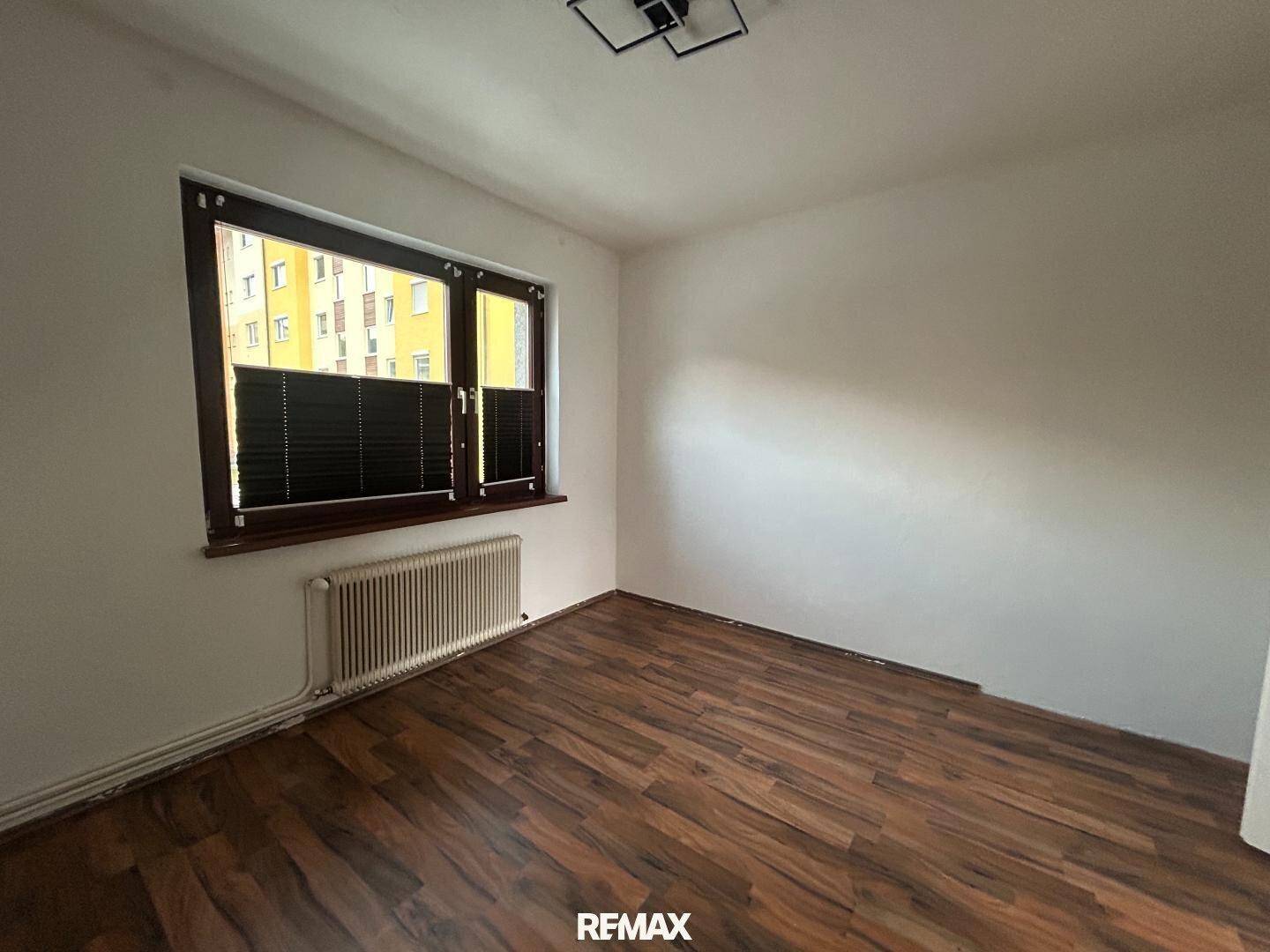 Helles Schlafzimmer mit dunklem Laminatboden und einem Fenster, das viel Tageslicht bietet.