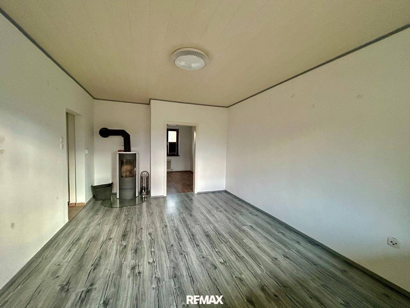 Geräumiges Wohnzimmer mit grauem Laminatboden und einem gemütlichen Holzofen in der Ecke.