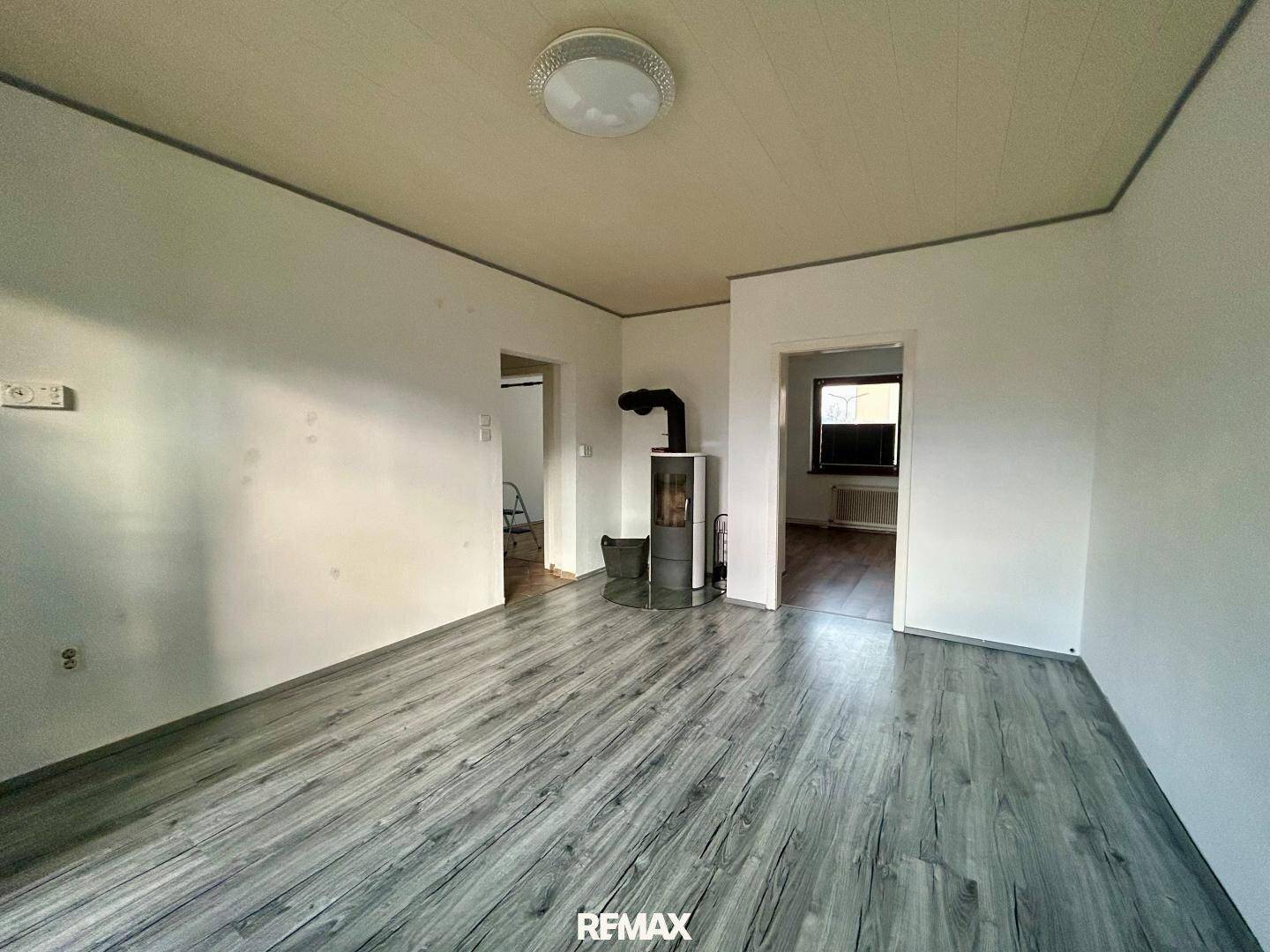 Heller Wohnbereich mit grauem Laminatboden und einem modernen Holzofen als Wärmequelle.