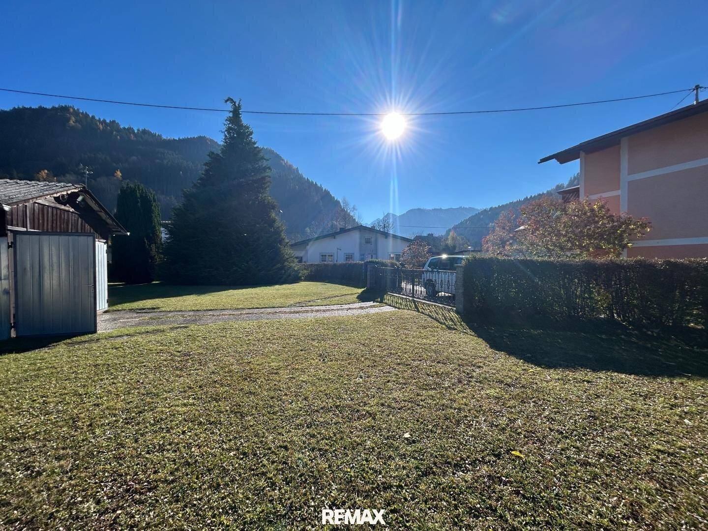 Sonnige Gartenfläche mit Hecke und weitem Blick auf die umliegende Berglandschaft.