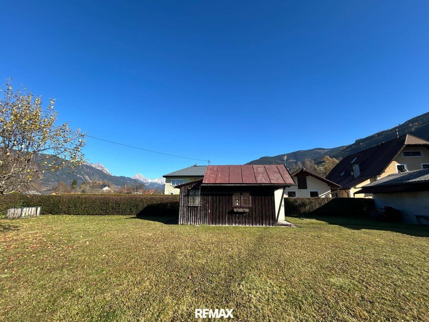 Weitläufiger Garten mit einem kleinen Holzschuppen und Panoramablick auf die Alpen.