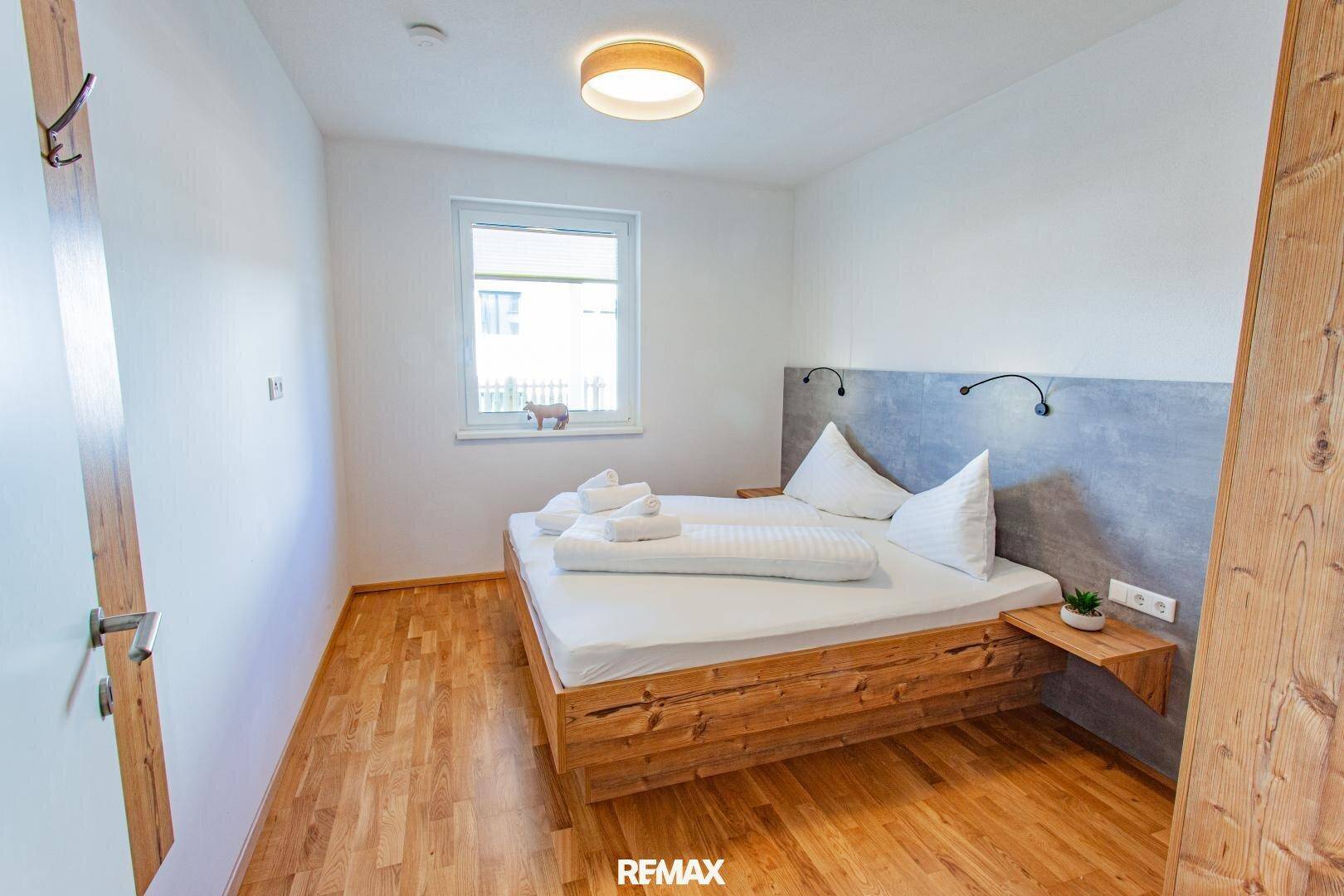 Gemütliches Schlafzimmer mit Holzbett, Holzboden und Fenster für natürliches Licht.