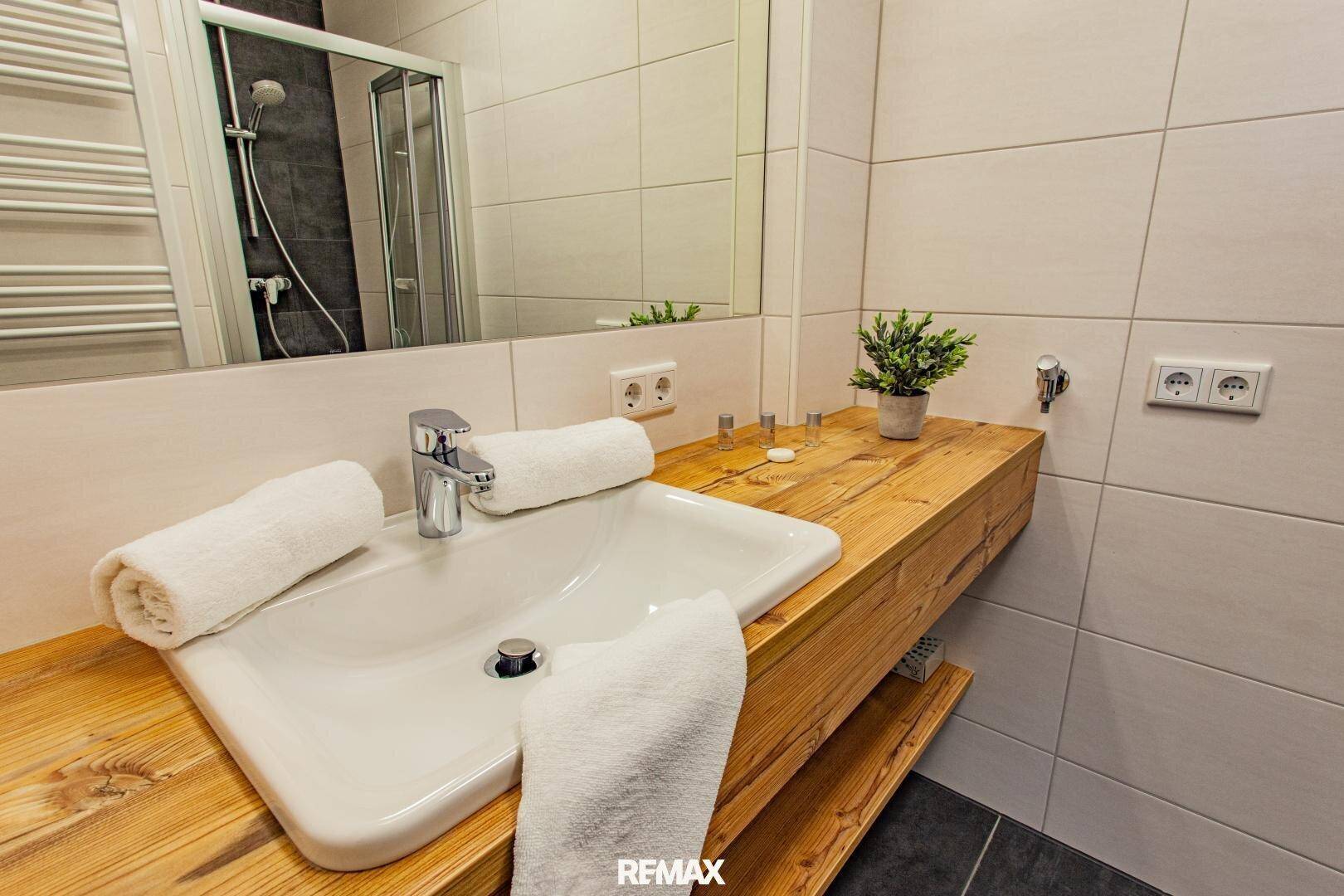 Modernes Badezimmer mit Holzwashbasin, großer Spiegelfläche und Duschkabine.