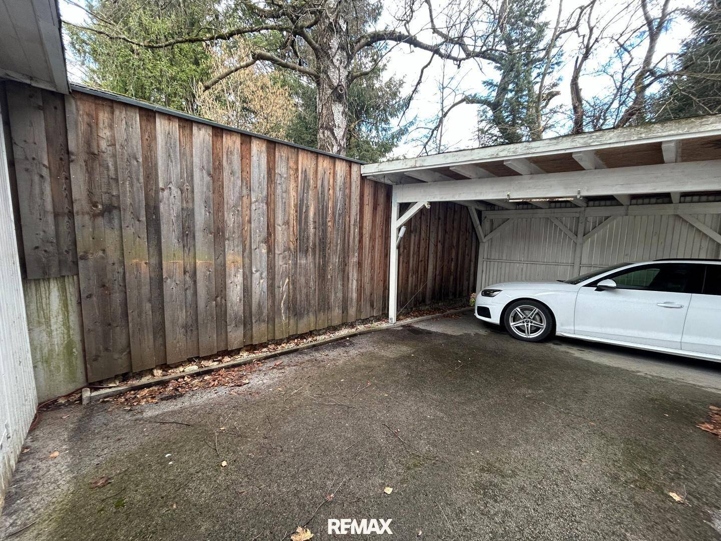 Überdachter Stellplatz (Carport) neben einem Holzschuppen, mit Auto geparkt.