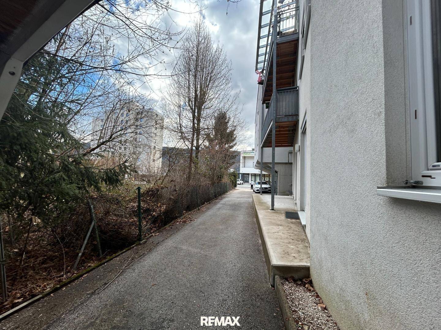 Schmaler Weg entlang des Gebäudes mit Blick auf die umliegende Bebauung.