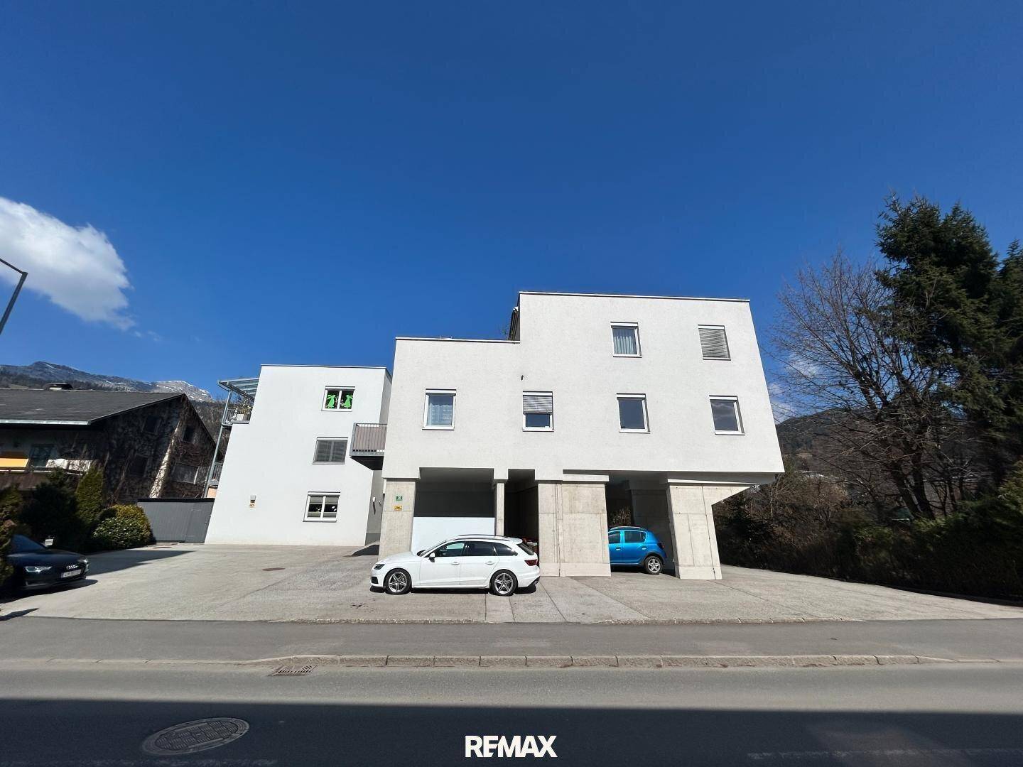 Modernes Mehrfamilienhaus mit weißer Fassade und Parkplätzen unter blauem Himmel.