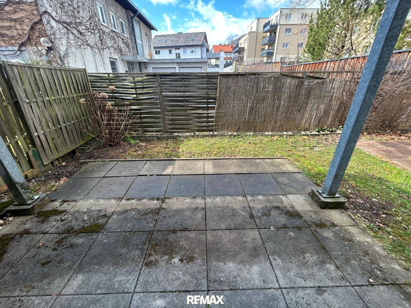 Gartenbereich mit gepflasterter Terrasse und Holzzaun, umgeben von Grün.