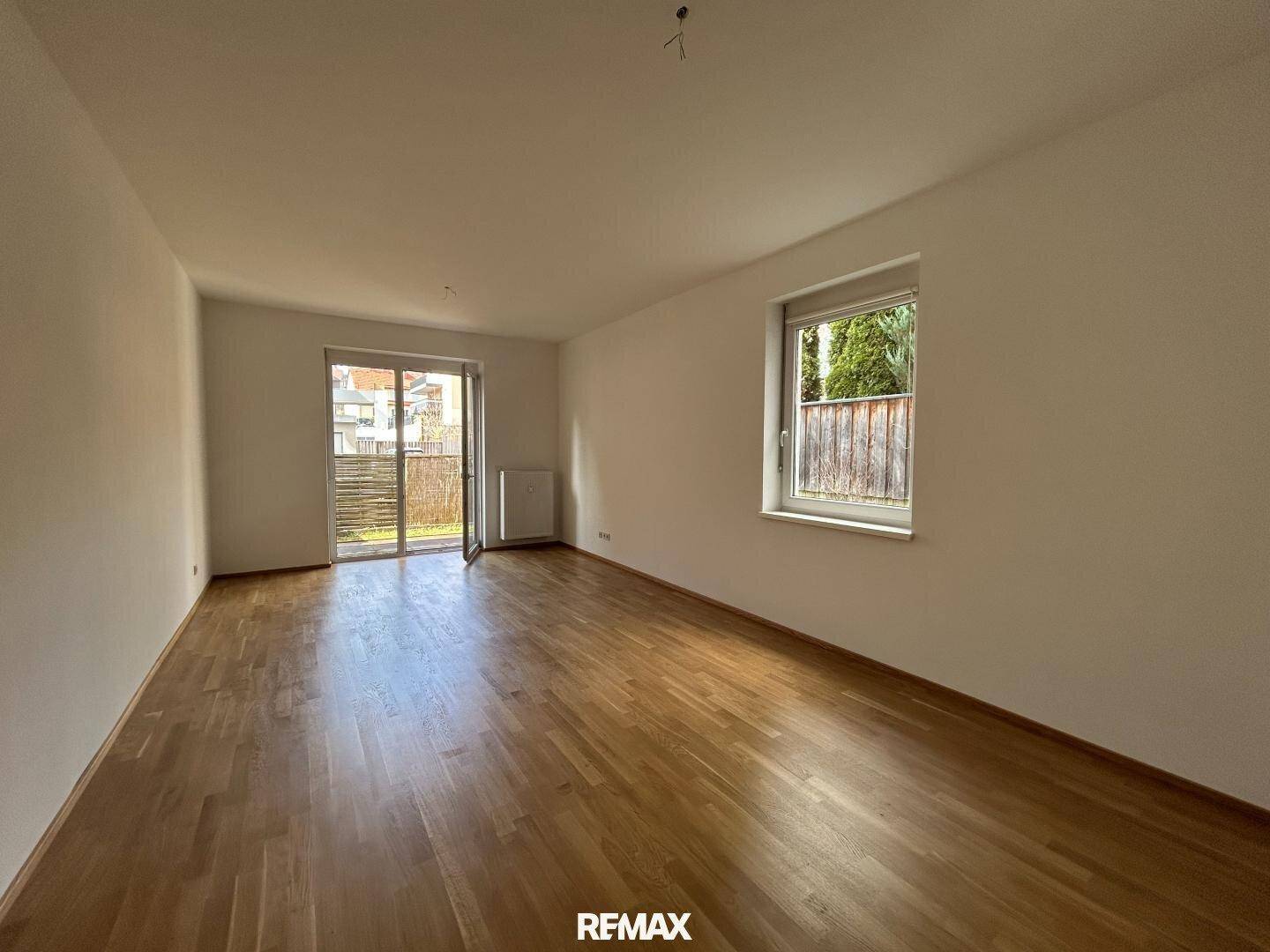Geräumiges Wohnzimmer mit Holzboden, Fenster und Zugang zu einem Außenbereich.