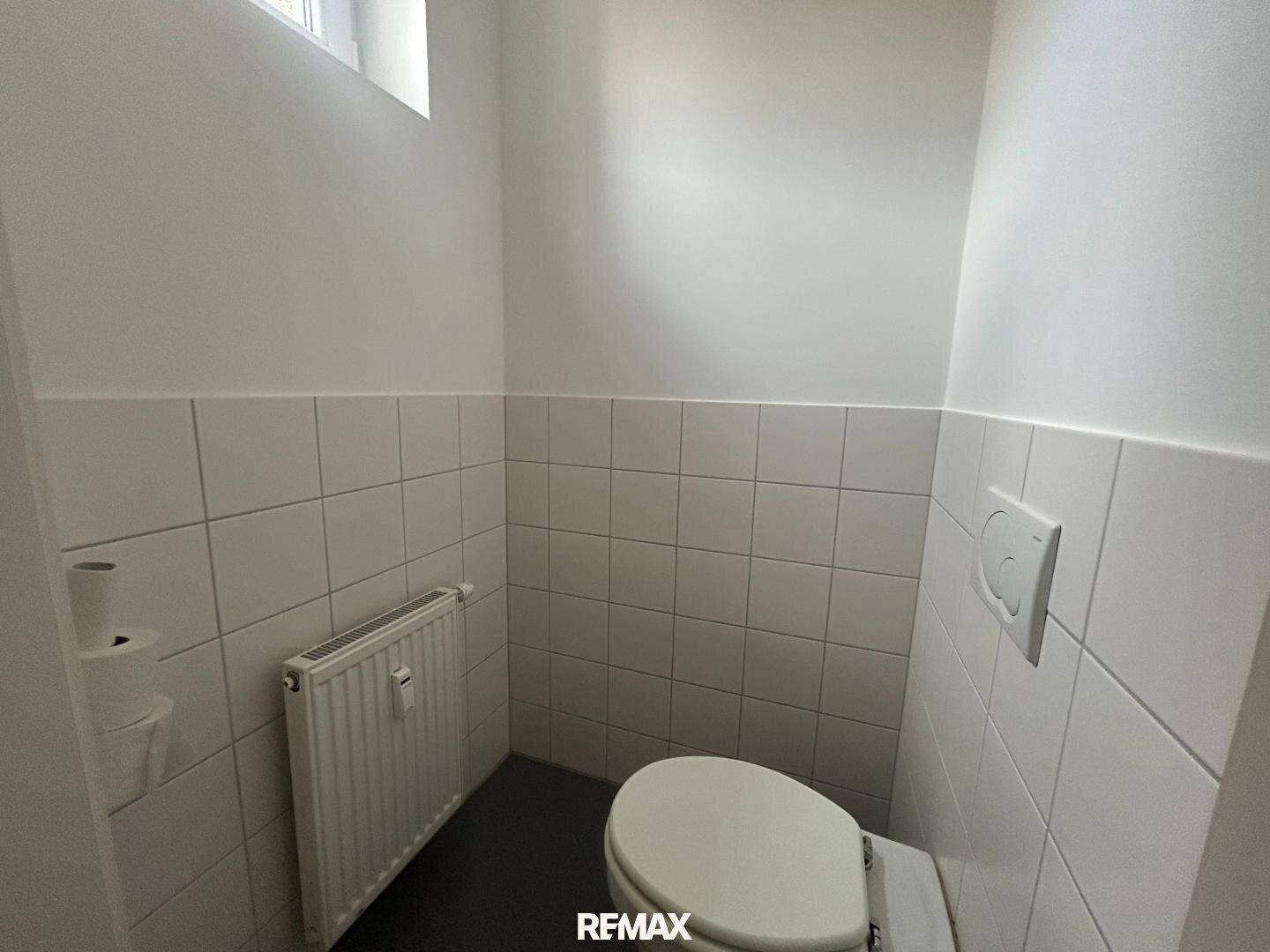 Kleines Gäste-WC mit Toilette, Heizkörper und weißen Wandfliesen.
