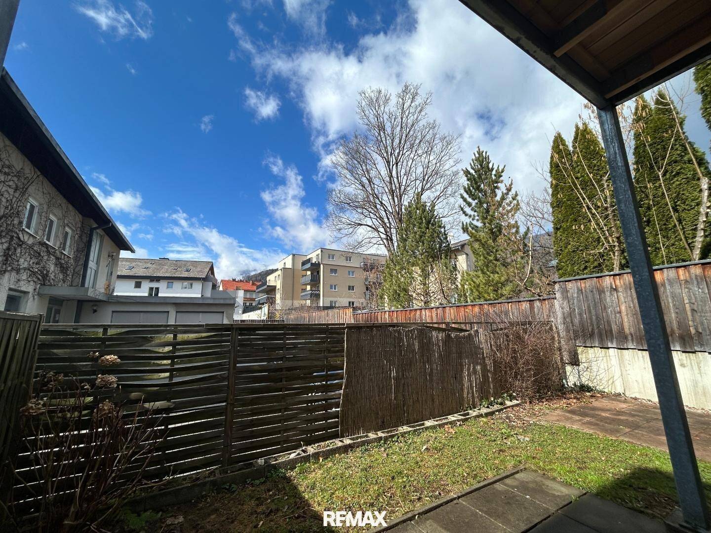 Garten mit Terrasse und Blick auf die Nachbarschaft unter bewölktem Himmel.