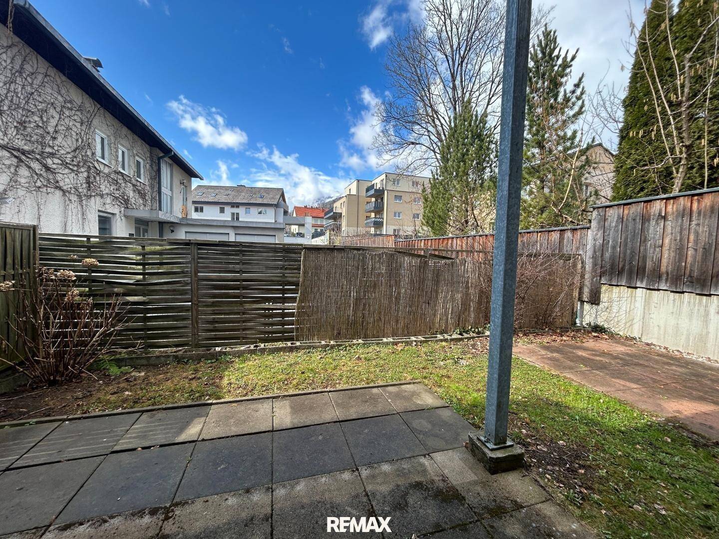 Garten mit Zaun und Blick auf die Nachbarschaft unter blauem Himmel.