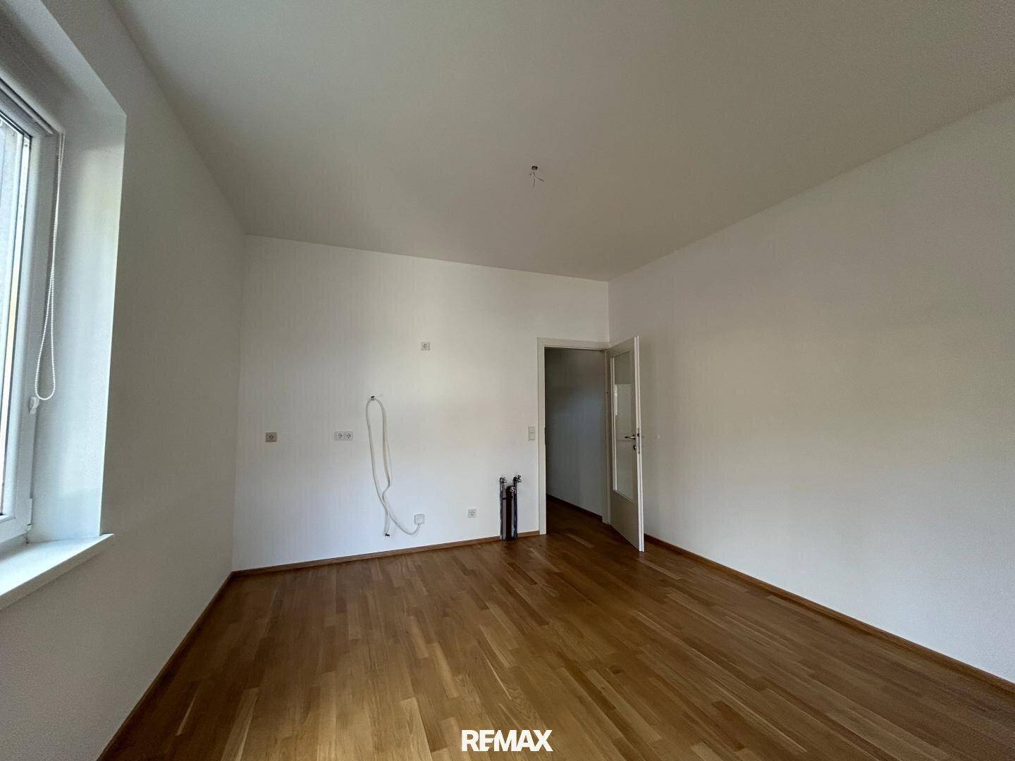 Helles Wohnzimmer mit Holzboden, weißen Wänden und Tür zu einem weiteren Raum.