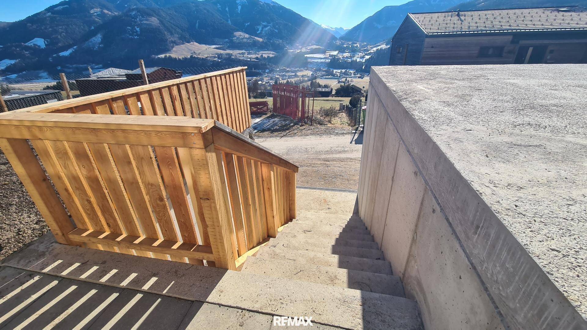 Außentreppe mit Holzgeländer, die zum Gebäude führt, mit Panoramablick auf die Berge.