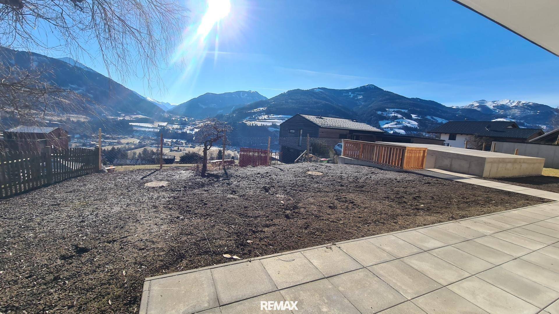 Sonniger Gartenbereich mit gepflasterter Terrasse und weitem Blick auf die umliegende Berglandschaft.