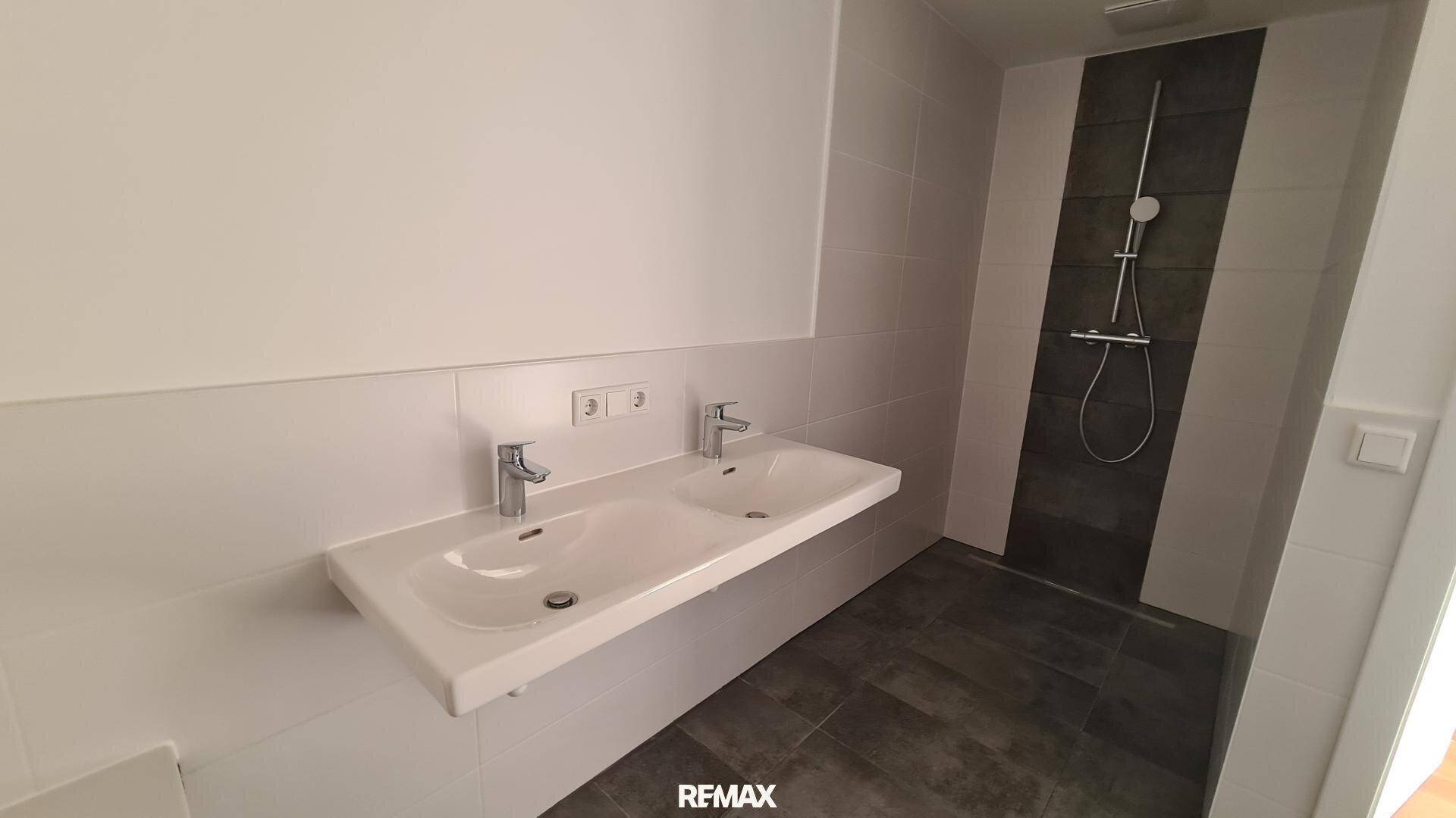 Helles Badezimmer mit Doppelwaschbecken und einer modernen, gefliesten begehbaren Dusche.