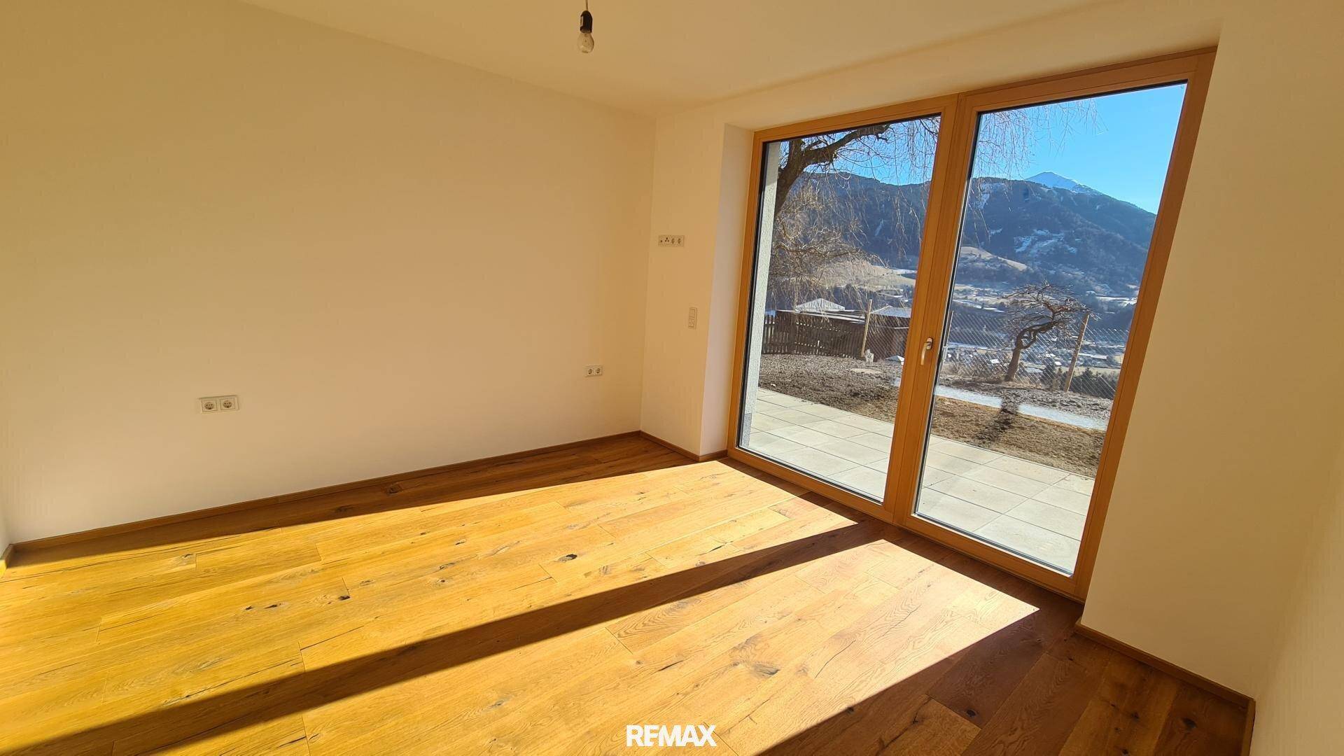 Heller Raum mit Holzboden und großem Fenster, das viel Tageslicht und einen schönen Bergblick bietet.